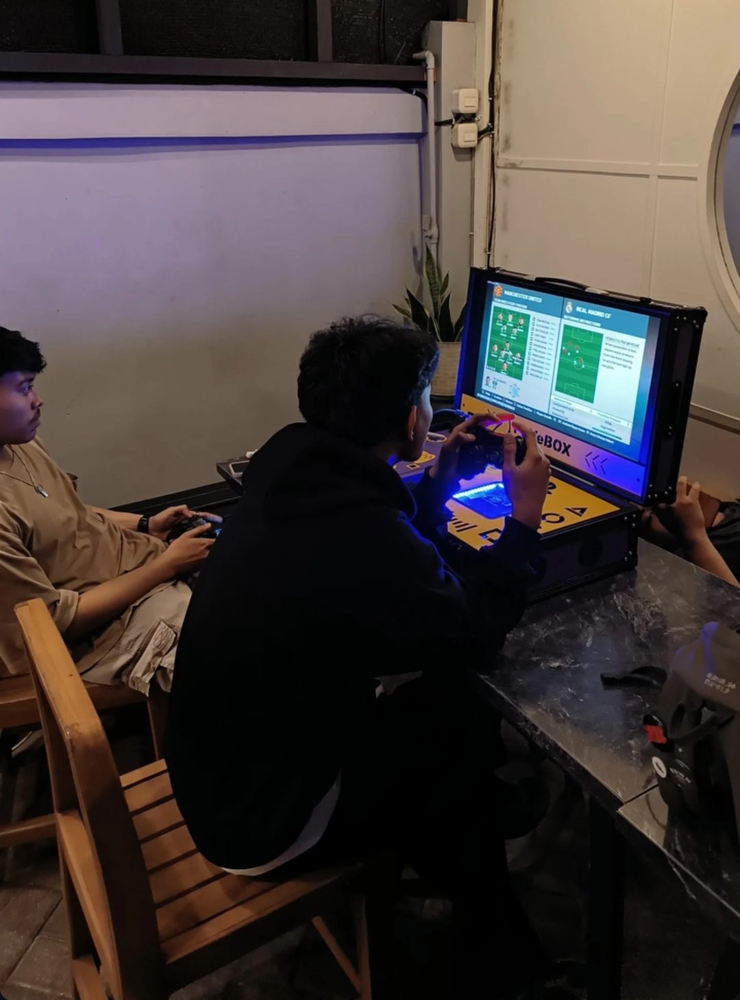 Dua orang bermain eFootball di unit PSVeBOX dalam kafe pada malam hari