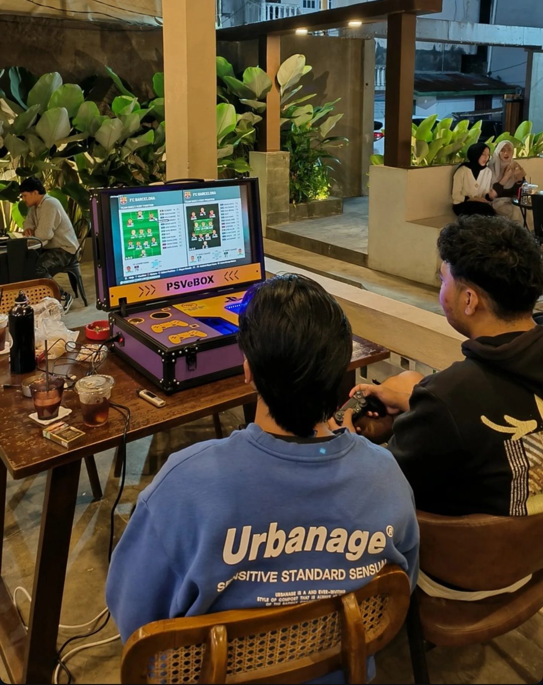 Unit PSVeBOX di kafe mitra, beberapa orang bermain di meja luar